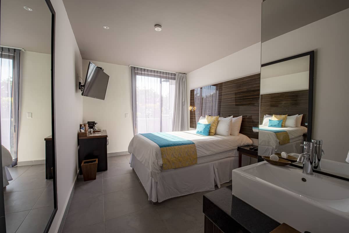 Een moderne hotelkamer met een groot bed, een nachtkastje, een aan de muur bevestigde televisie en een badkamer met een wastafel en spiegel.