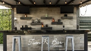 Um bar com balcão de madeira, duas televisões fixadas na parede e uma placa com o dizeres "Tian Bar".