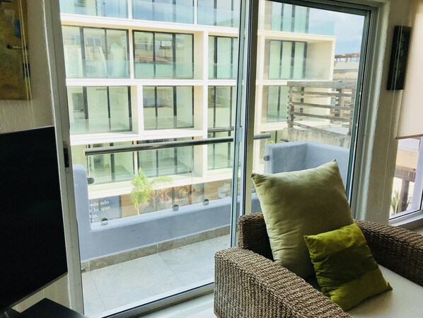 A room with a large window, a sofa with cushions, and a television.