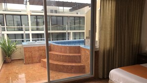 Une chambre d’hôtel avec une grande fenêtre, un lit, une petite table et une plante en pot.