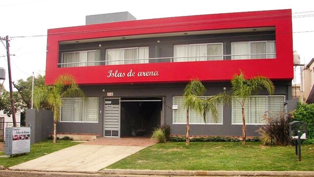 A two-story building with a red facade and the name "Islas de arena" on the front. - Islas De Arena (Colon)