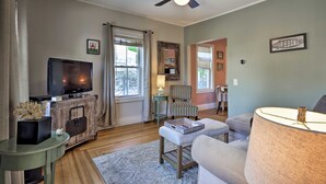 Un salon comprenant un téléviseur, un ventilateur de plafond, un meuble en bois, un fauteuil à rayures et une lampe.