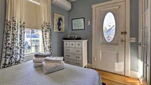 Une chambre à coucher comprenant un lit, une commode, une fenêtre avec des rideaux, une porte avec un vitrage et des œuvres d’art murales.