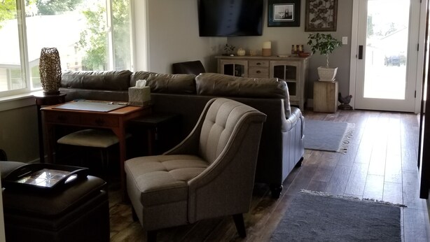 Una sala de estar con un sofá seccional, una mesita, una silla, un televisor y un mueble bajo.