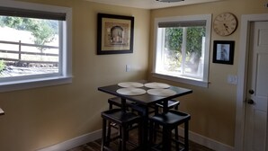 Un comedor con una mesa, sillas, dos ventanas, un cuadro enmarcado, un reloj y una puerta.
