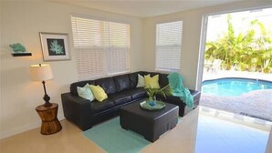 Un salón con un sofá negro, una mesita auxiliar, una lámpara y vistas a una piscina.