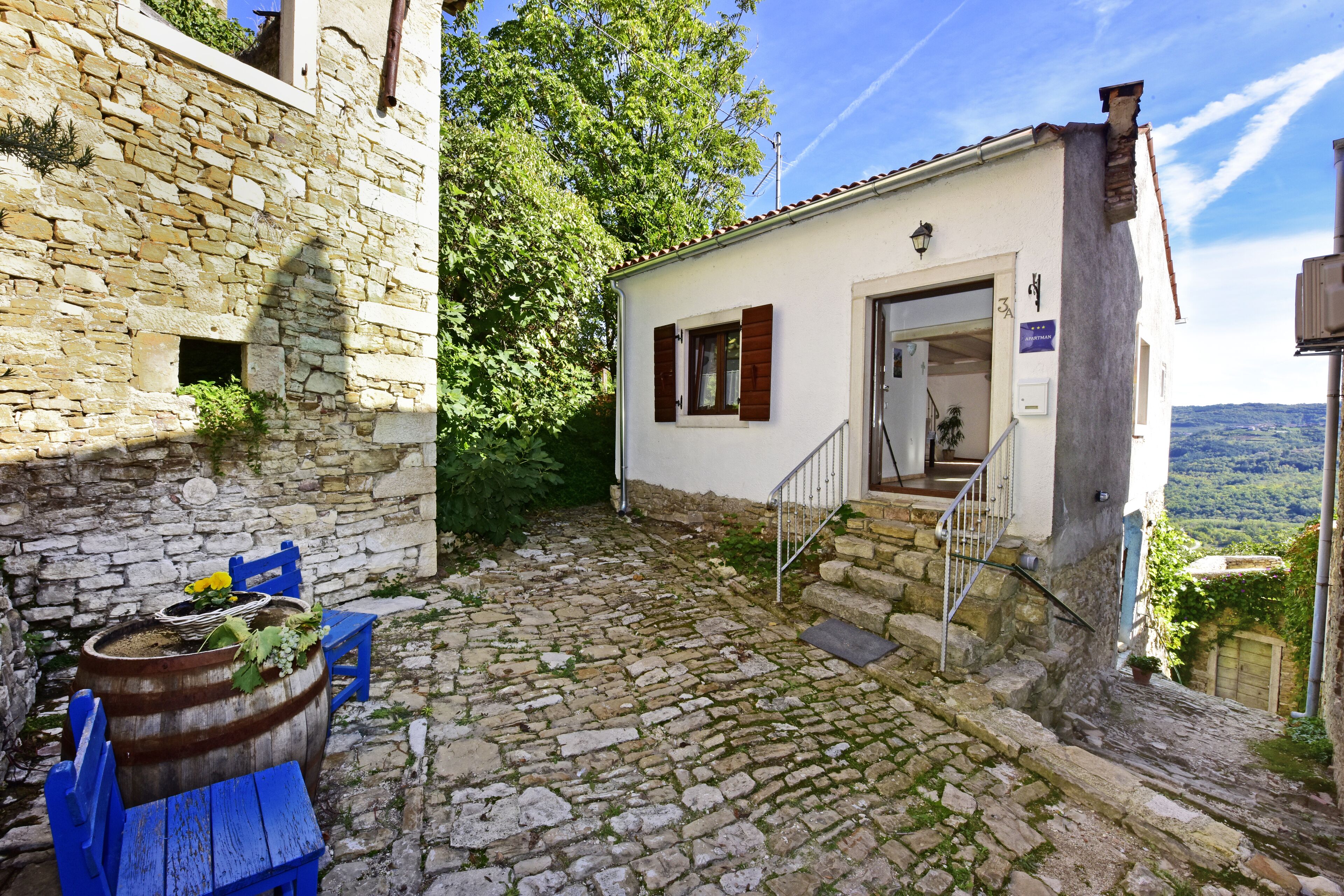 A stone building with a rustic exterior, a wooden barrel table with plants, and a staircase leading to a door.