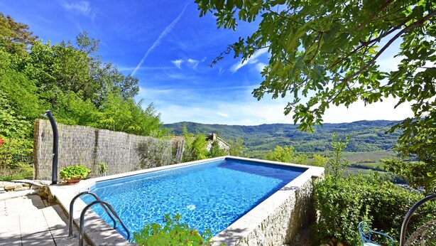 A rectangular swimming pool with a stone border, surrounded by lush greenery and a scenic view of hills. - Villa Fragola beautiful house whit pool and panoramic view (Motovun)