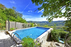 A rectangular swimming pool with a stone border, surrounded by lush greenery and a scenic view of hills. - Villa Fragola beautiful house whit pool and panoramic view (Motovun)