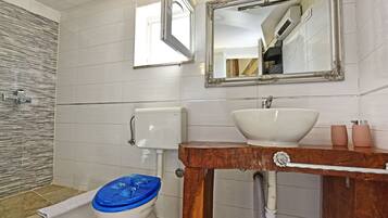 Une salle de bain avec des toilettes blanches, un meuble-lavabo en bois doté d’un grand évier et un miroir au-dessus du meuble-lavabo.