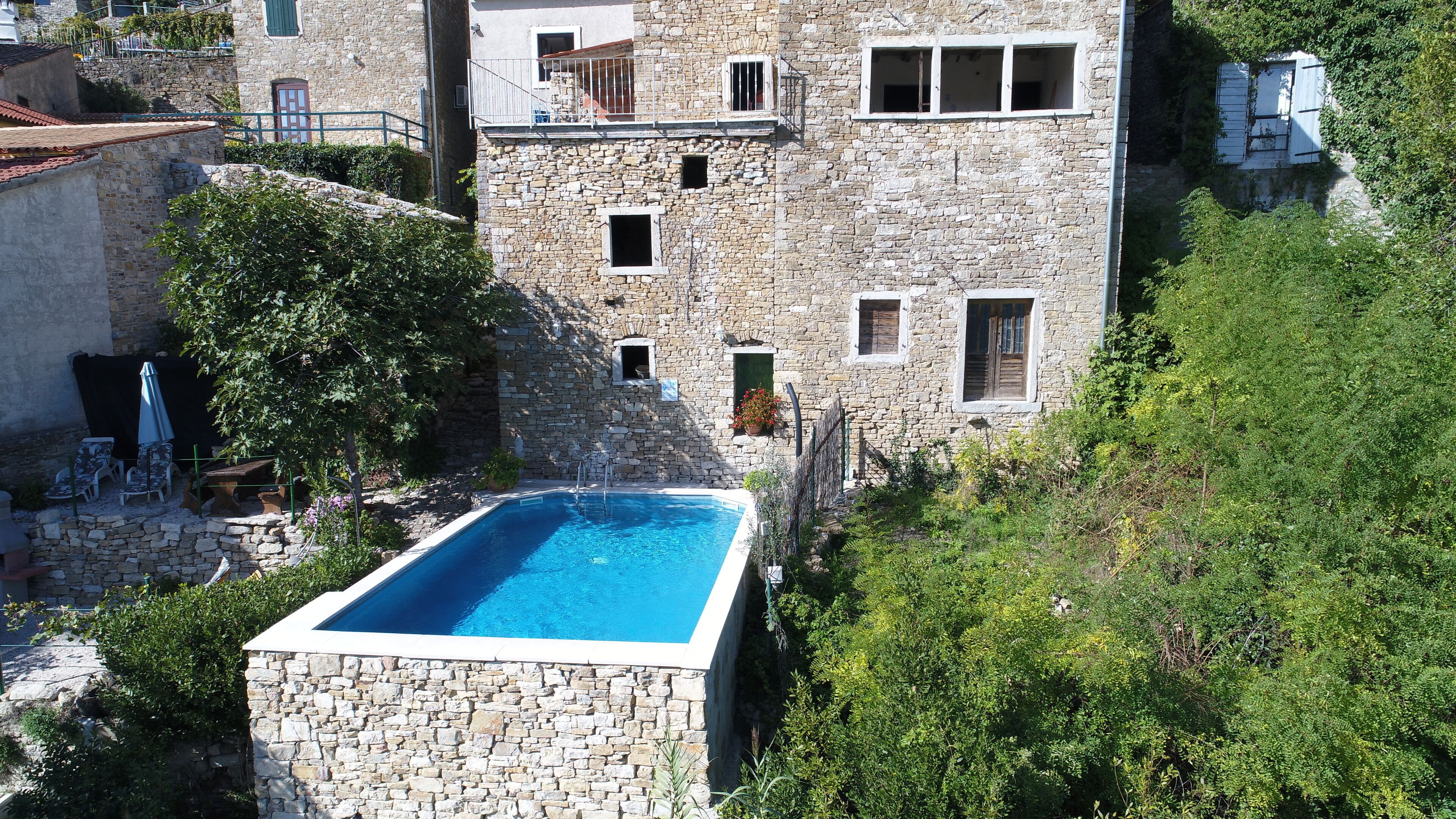 Ein Steinhaus mit rechteckigem Pool, umgeben von Grünflächen und einer Steinmauer.