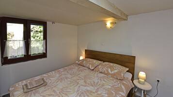 A bedroom with a bed, a nightstand, a lamp, a window with curtains, and a wall-mounted light fixture.