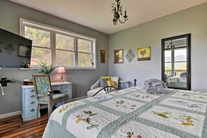 A bedroom with a large bed, a desk, a chair, a dresser, and a window with a view of trees.