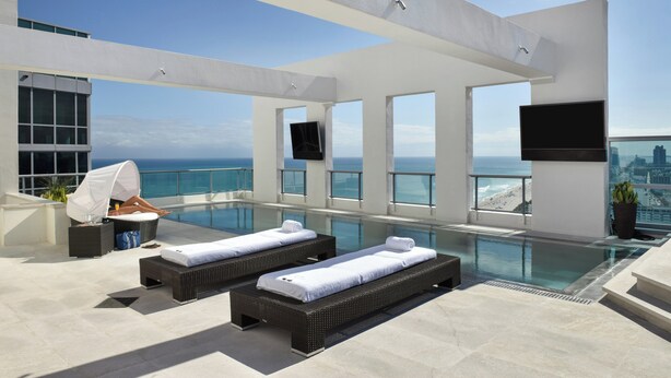 A rooftop infinity pool with two sun loungers, a flat-screen TV, and a city view. - Setai (Miami Beach)