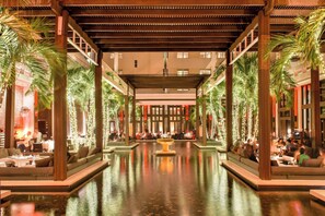A spacious indoor area with a central water feature, seating areas on both sides, and a modern architectural design with wooden beams and columns. - Setai (Miami Beach)