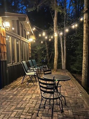 An outdoor patio with brick flooring, metal chairs, and a round table. - Black Bear Lodge: Fall Colors on the Au Sable | Cozy Riverfront Cabin (Frederic)