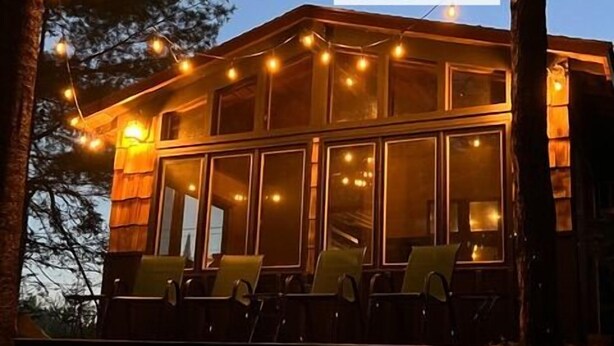 A cabin with a sign for Freshwater Vacation Rentals, featuring a deck with chairs and string lights. - Black Bear Lodge: Fish, Hike, and Relax in Michigan's Summer Paradise (Frederic)