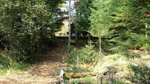 A forested area with a dirt path leading to a building with outdoor seating. - Black Bear Lodge: Fish, Hike, and Relax in Michigan's Summer Paradise (Frederic)