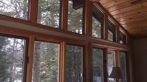 A room with large windows, wooden ceiling, and a lamp. - Black Bear Lodge: Fish, Hike, and Relax in Michigan's Summer Paradise (Frederic)