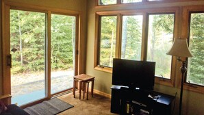 A room with large windows, a television, and a lamp. - Black Bear Lodge: Fish, Hike, and Relax in Michigan's Summer Paradise (Frederic)