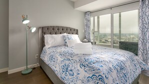 Une chambre d’hôtel avec un grand lit, une lampe sur pied et une vue sur la ville par une grande fenêtre.