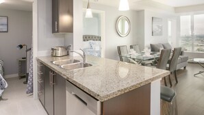 Une cuisine moderne dotée de plans de travail en granit, d’appareils électroménagers en acier inoxydable et d’un coin repas avec une table et des chaises en verre.
