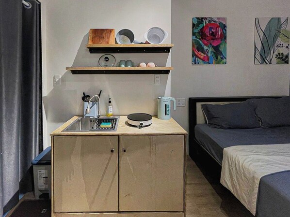 Une pièce de taille modeste comprenant un coin cuisine, un lit et des œuvres d’art accrochées aux murs.