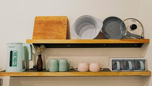 A kitchen shelf with a coffee maker, two mugs, a wooden cutting board, a stone grinder, and a spice container. - Tranquil Studio with Kitchen near Airport in bustling area (Ho Chi Minh City)