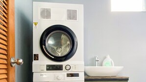 A stacked washer and dryer unit in a room with a tiled floor, a wooden door, and a window. - Tranquil Studio with Kitchen near Airport in bustling area (Ho Chi Minh City)