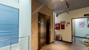 An interior corridor with a wooden wall, an elevator, a fire extinguisher, and a sign indicating an exit. - Tranquil Studio with Kitchen near Airport in bustling area (Ho Chi Minh City)