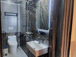 Une salle de bain moderne avec un mur en marbre, un lavabo blanc et une douche dotée d’une paroi en verre.