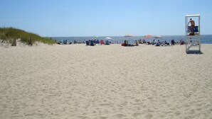 A beach with a lifeguard tower, umbrellas, and people relaxing. - Walk to family friendly beach in West Dennis! (Dennis)