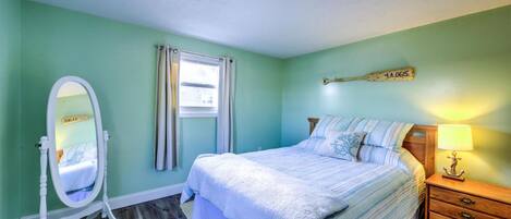 A bedroom with a bed, a vanity with a mirror, a window with curtains, and a nightstand with a lamp.
