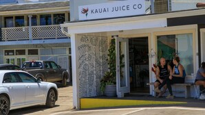 Ein Laden mit einem Schild, das "Kauai Juice Co." zeigt, und einer Wand mit dekorativen Pflanzenabbildungen.