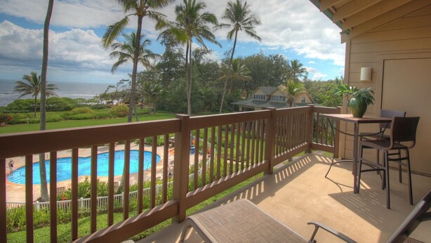 Ein Balkon mit Blick auf einen Swimmingpool, Palmen und ein Haus im Hintergrund.