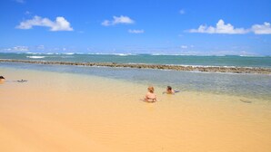 Ein Strand mit klarem Wasser, einem steinernen Mole und einem sandigen Ufer.