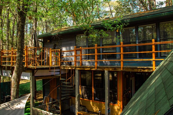 A cabin with a wooden deck, a staircase, and a large window overlooking a forest.