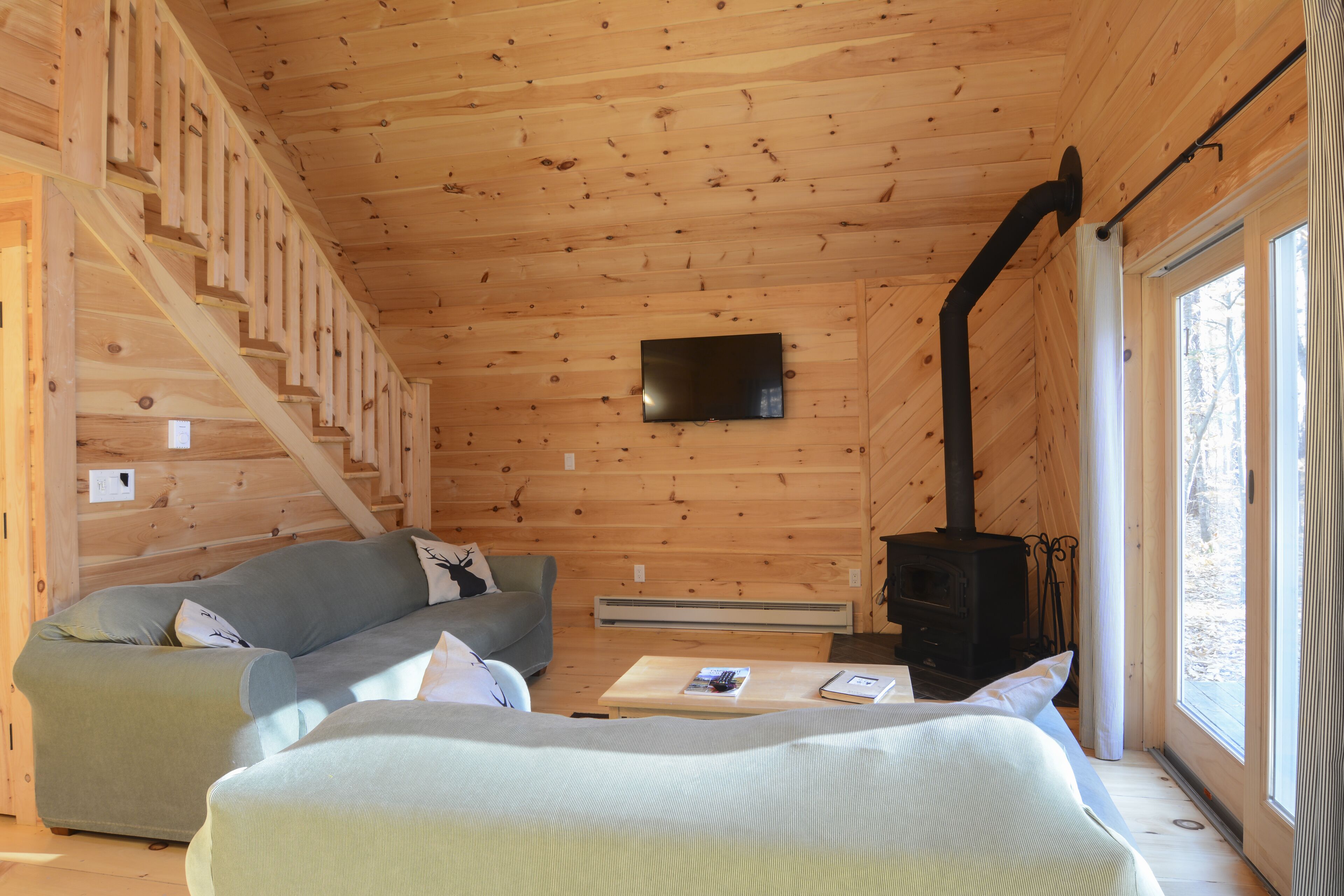 L’intérieur d’un chalet en bois comprend un escalier, un canapé, un lit, une cheminée et un téléviseur fixé au mur.