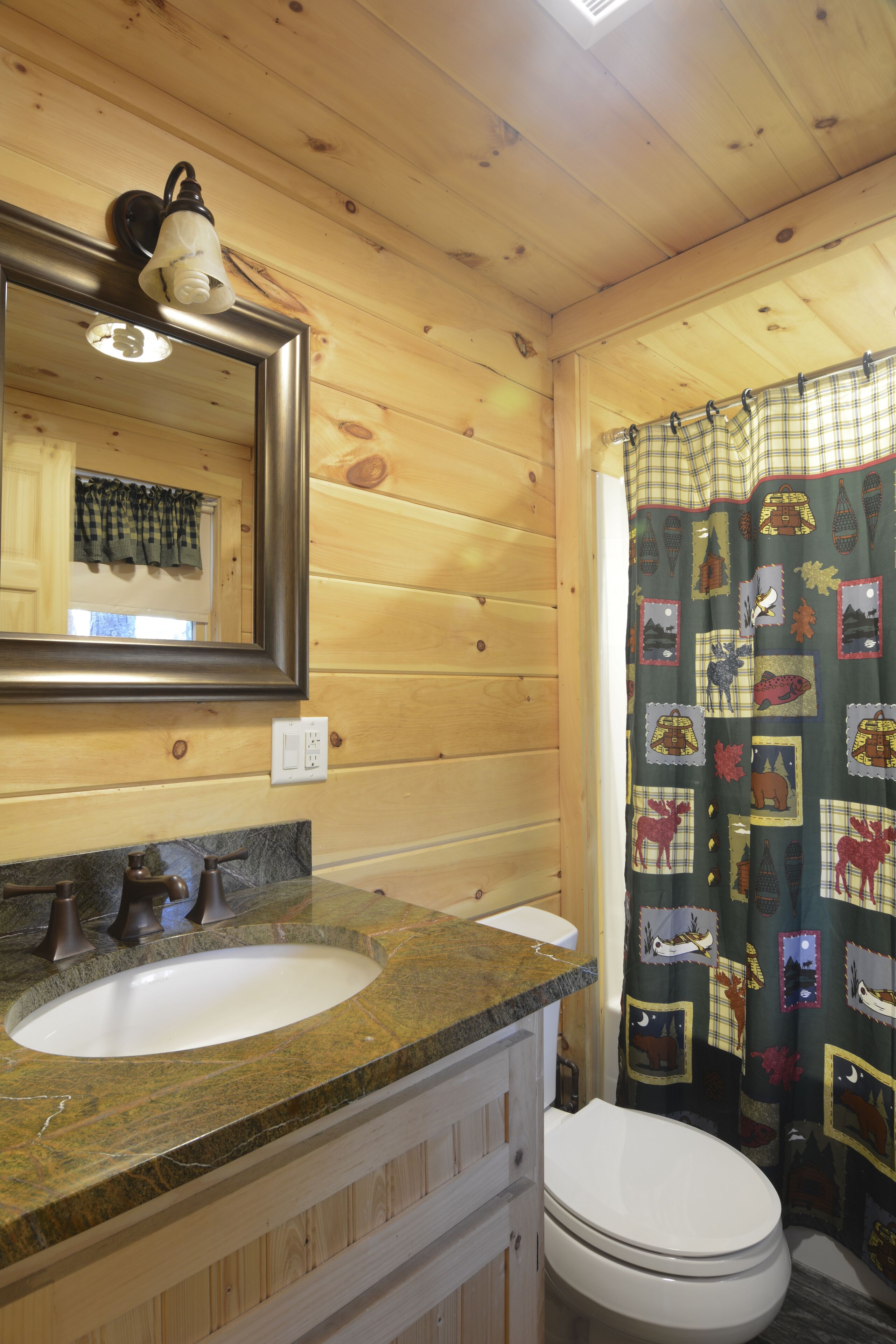 Un baño de cabaña de madera con lavamanos de granito, un inodoro y un espejo.
