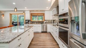 A modern kitchen with white cabinetry, stainless steel appliances, a granite countertop, and a wooden floor. - Hot Tub, Pickleball, Covered Deck at Remodeled Gem (Leavenworth)