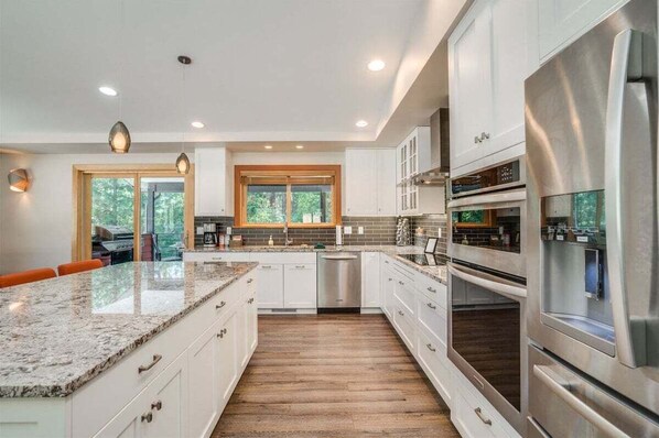 A modern kitchen with white cabinetry, stainless steel appliances, a granite countertop, and a wooden floor.