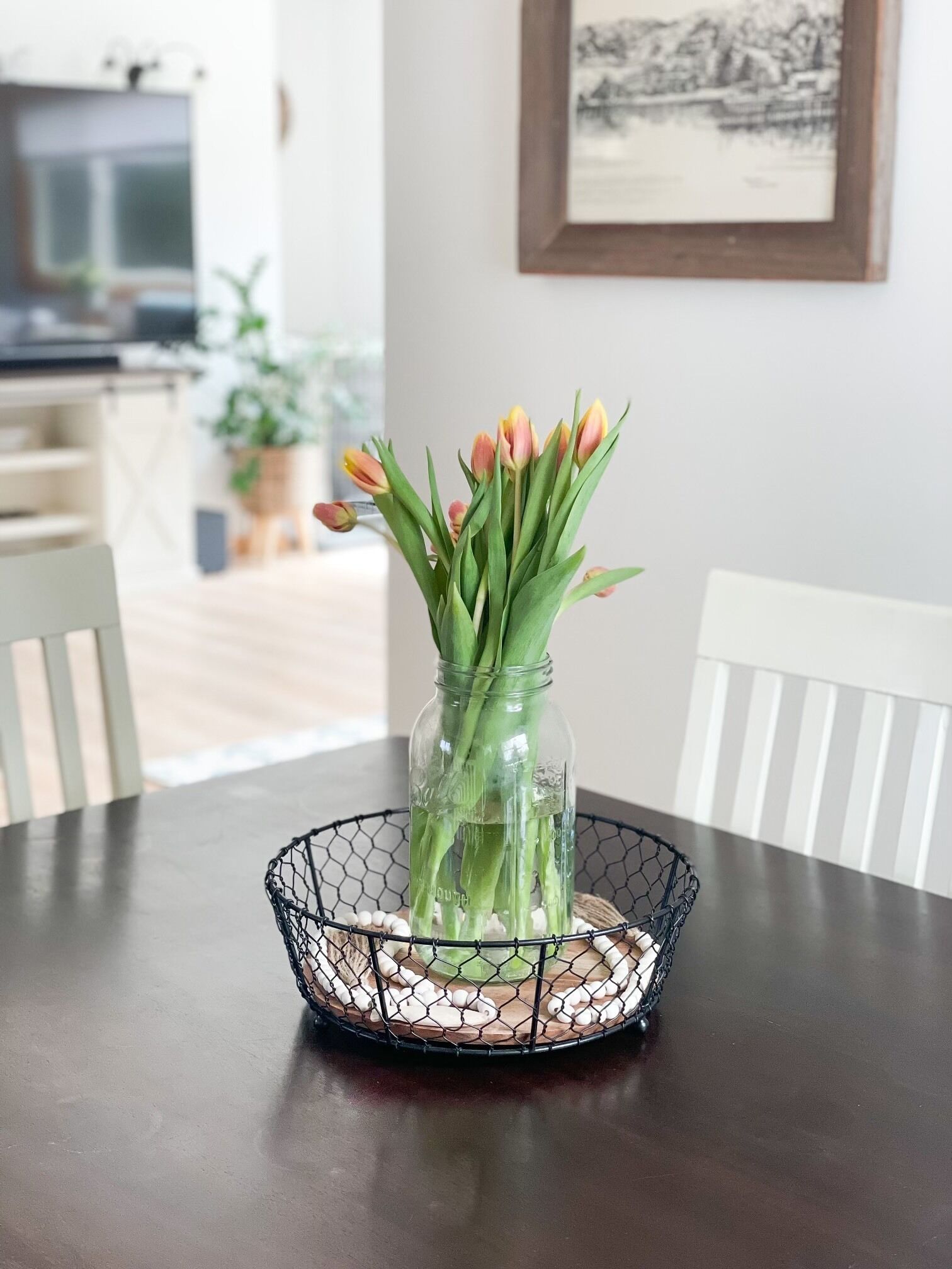 A clear glass vase with tulips on a wire basket on a table.