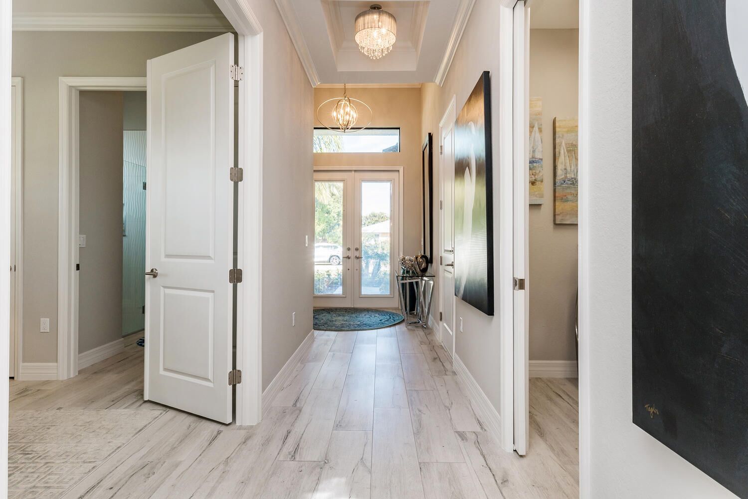 A hallway with a light wooden floor, white doors, and a chandelier.