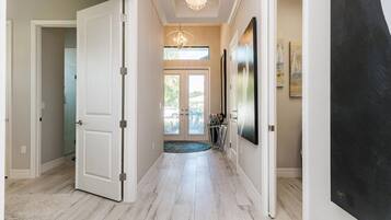 A hallway with a light wooden floor, white doors, and a chandelier.