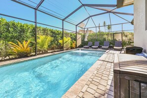 Un espace piscine avec une eau d’un bleu cristallin, entouré d’une structure en verre, et aménagé avec des chaises longues et un foyer.