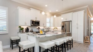 Una cocina moderna con armarios blancos, electrodomésticos de acero inoxidable e isla de mármol con taburetes de bar.