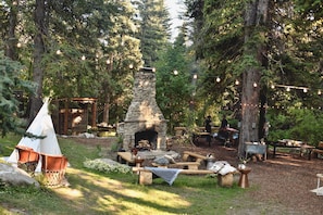 Surrounded by nature, this cozy outdoor space features a stone fireplace, a rustic bench, and a small table.