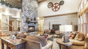 A spacious living room with a stone fireplace, comfortable seating, a television, and a staircase leading to an upper level. - BOULDER RIDGE - 7 BD, HUGE THEATER, POOL TABLE, HOT TUB, SAUNA (Sundance)