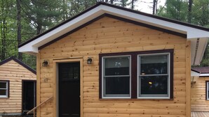 A wooden cabin with a front door, two windows, and a small porch.