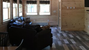 A cabin interior with a wooden ceiling, a ceiling fan, a sofa, a dining table, and a patterned floor.